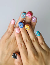 Hand model wearing short squoval press-on nails with playful 3D flowers, hearts, and multicolor googly eyes